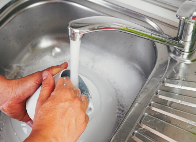 Young man's hands washing a white cup with water and dish soap. Close up shot of a man's hands rinsing a cup that was dirty and used. Concept of cleanliness