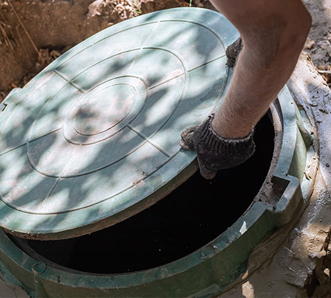 The man opens the sewer hatch. Installation and maintenance of septic tanks