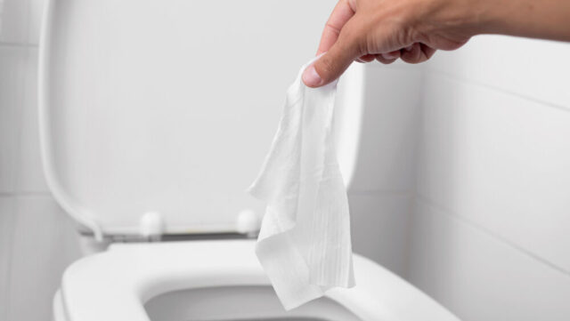 Throwing a wet wipe into the toilet in a white-tiled restroom