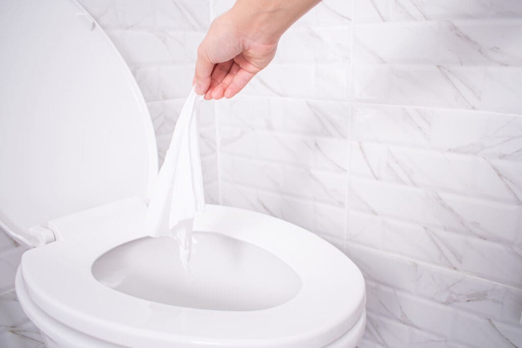 A hand throwing a wipe into the toilet.