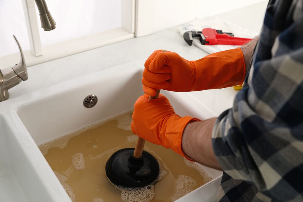 A person wearing orange gloves and plunging a clogged sink.