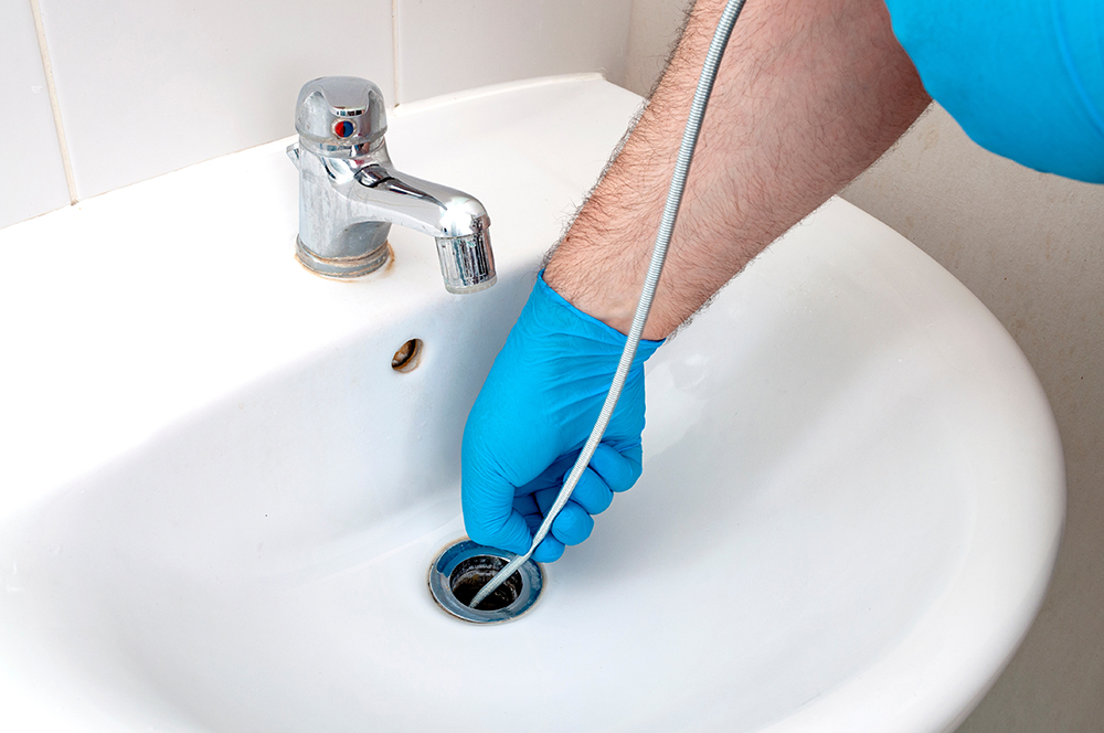 A plumber in blue gloves snaking a sink drain.