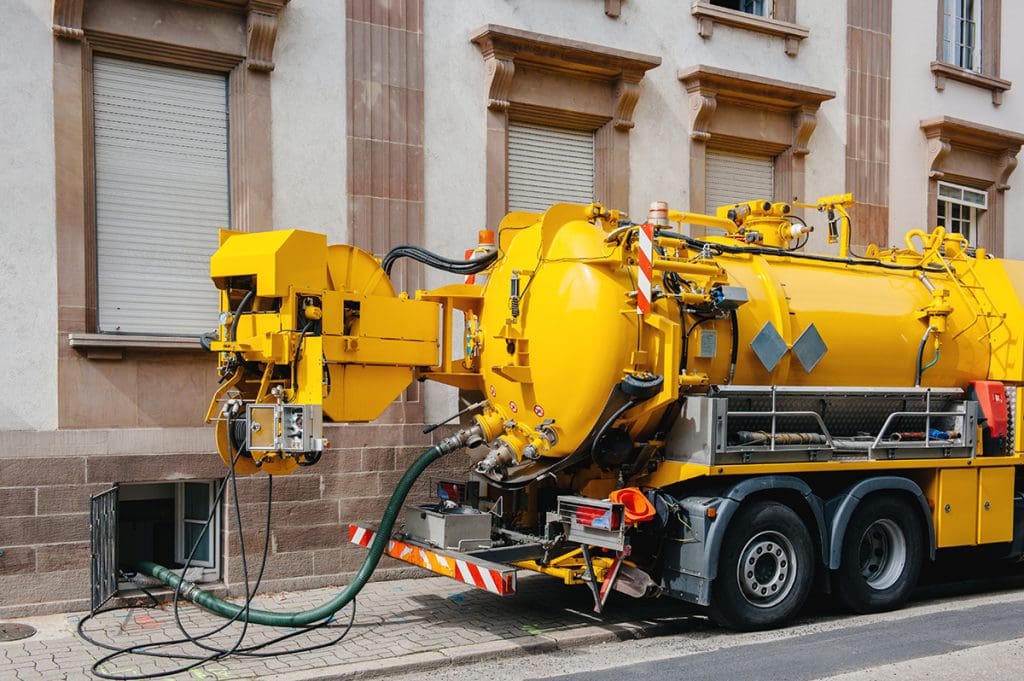 A yellow sewage truck pumping grease from a restaurant’s grease trap.