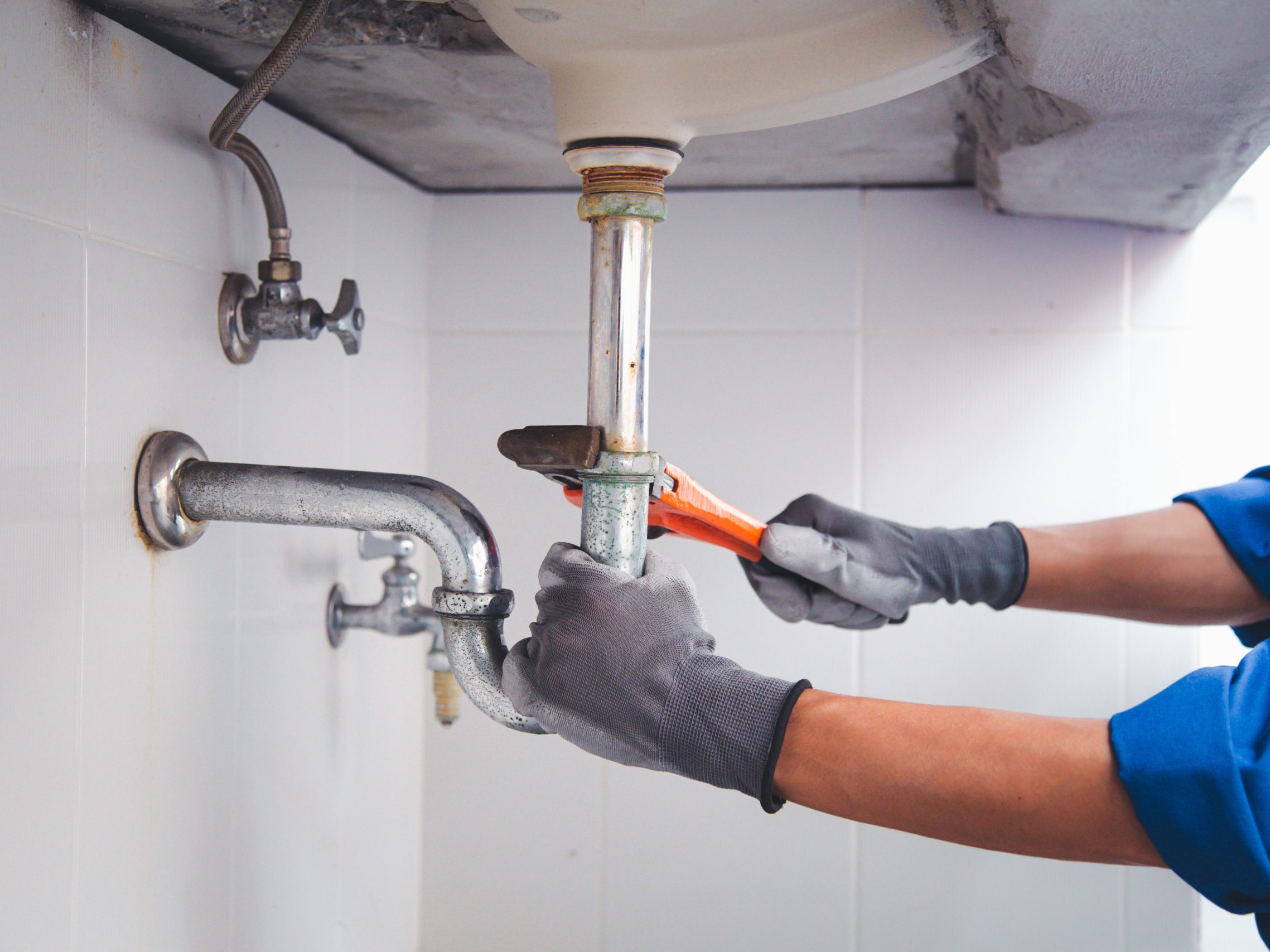 A person works on the pipes below a sink.