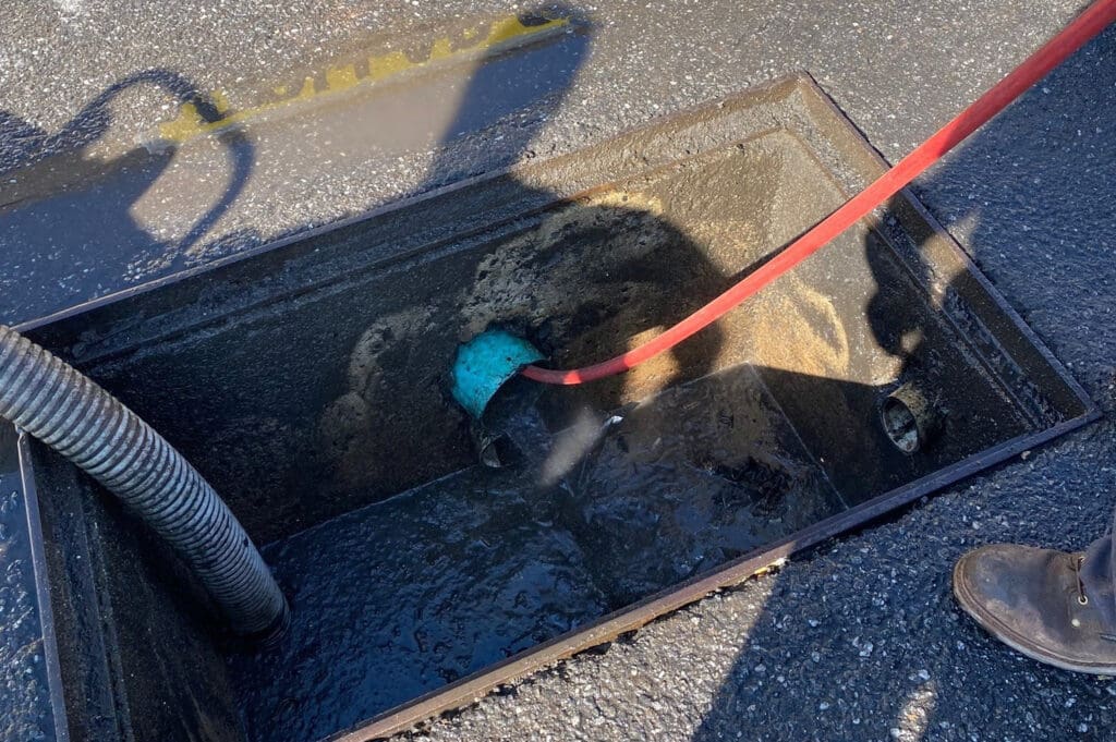 A pair of septic maintenance professionals pumping a sewage drain pipe.