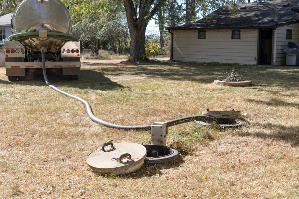 Septic pumping truck connected to underground tank at a residential property during routine maintenance service.