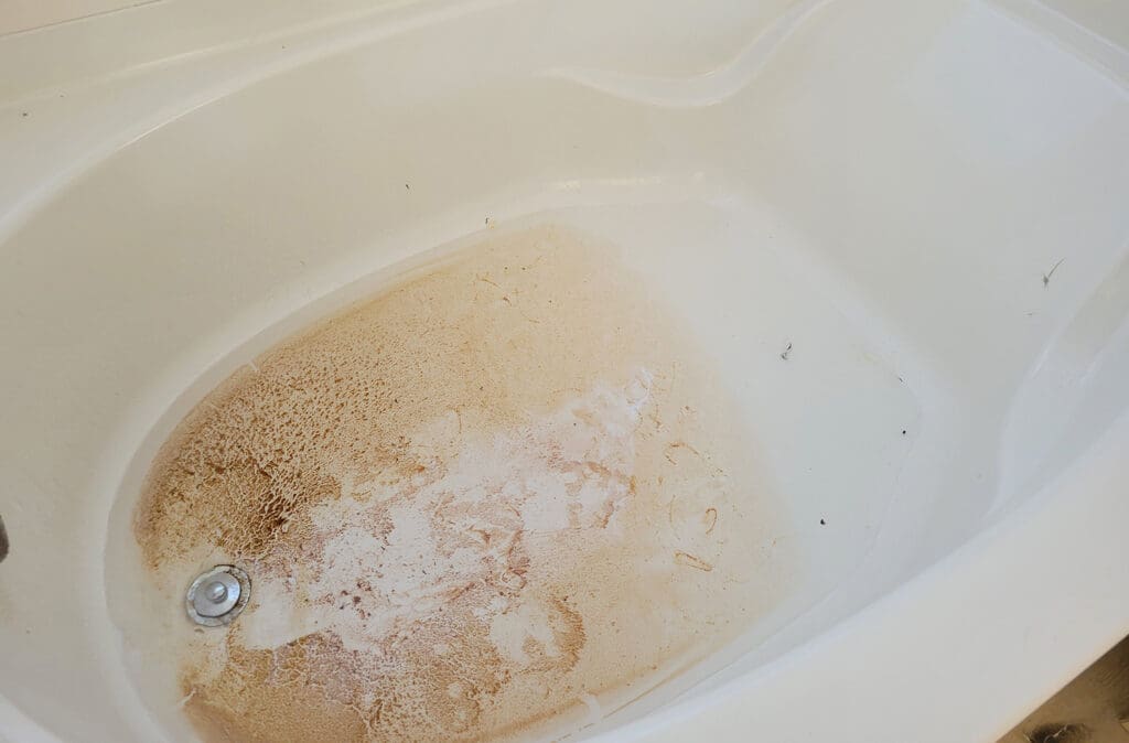 A backed-up bathtub with dirt on the bottom.