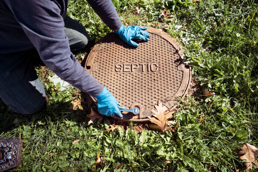 A person opening a septic tank, wearing blue gloves while doing so